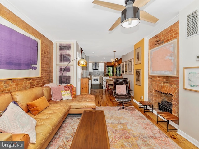 living area with wood finished floors, a brick fireplace, a ceiling fan, brick wall, and baseboards