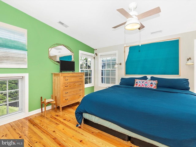 bedroom with wood finished floors, multiple windows, a ceiling fan, baseboards, and lofted ceiling
