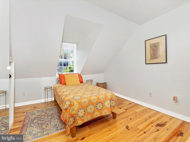 bedroom with wood finished floors, lofted ceiling, and baseboards