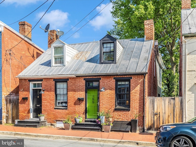 cape cod home with brick siding, fence, a chimney, and a standing seam roof