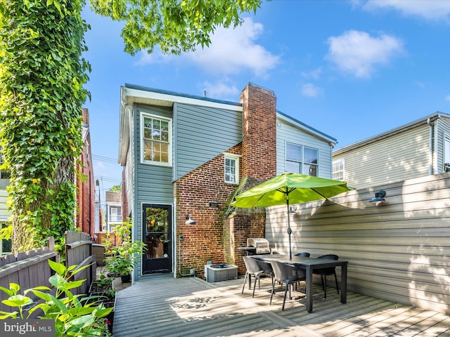 rear view of property featuring a wooden deck, fence, a chimney, central AC, and outdoor dining area