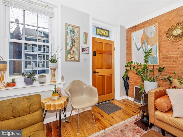 sitting room featuring brick wall, wood finished floors, and baseboards
