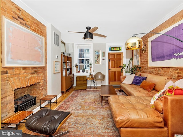 living area with a ceiling fan, wood finished floors, brick wall, and a fireplace