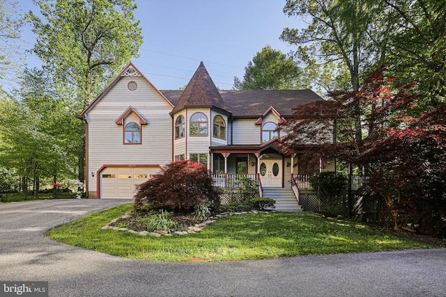 victorian home featuring a porch, driveway, a front lawn, and a garage