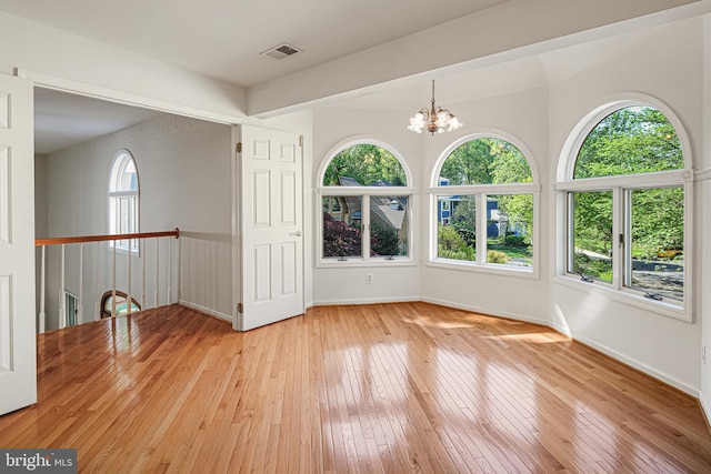empty room featuring baseboards, a chandelier, light wood-style flooring, and a wealth of natural light