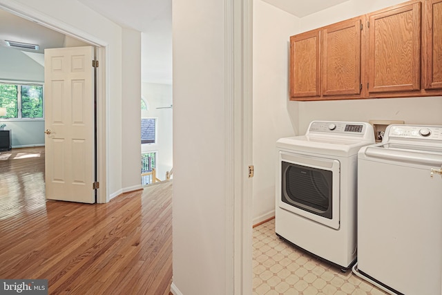 clothes washing area with visible vents, baseboards, light wood-style floors, separate washer and dryer, and cabinet space
