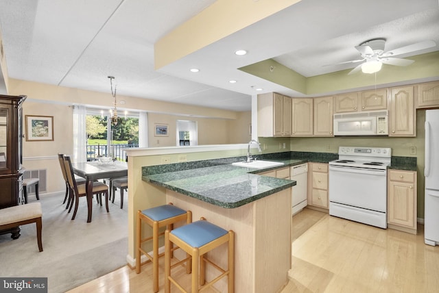 kitchen featuring a peninsula, light brown cabinetry, white appliances, a kitchen bar, and a sink