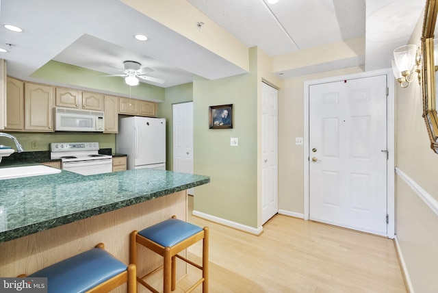 kitchen with a sink, light wood finished floors, dark countertops, and white appliances