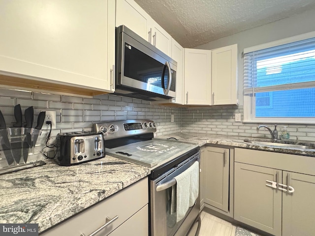 918 Hillside Ave, Upper Chichester, PA 19061 - kitchen with decorative backsplash, a textured ceiling, light stone counters, a sink, and appliances with stainless steel finishes