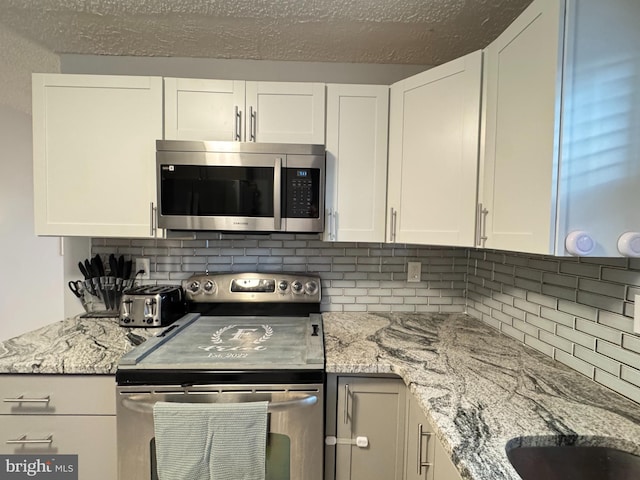 918 Hillside Ave, Upper Chichester, PA 19061 - kitchen featuring light stone counters, a textured ceiling, stainless steel appliances, white cabinetry, and tasteful backsplash