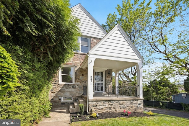 bungalow-style house featuring stone siding, a porch, and fence