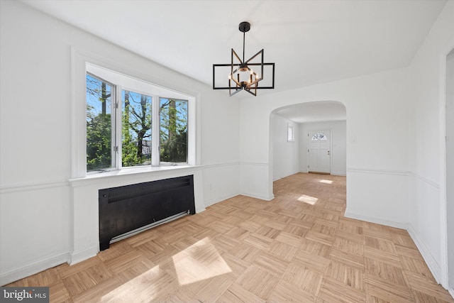 unfurnished dining area with radiator, a chandelier, baseboards, and arched walkways