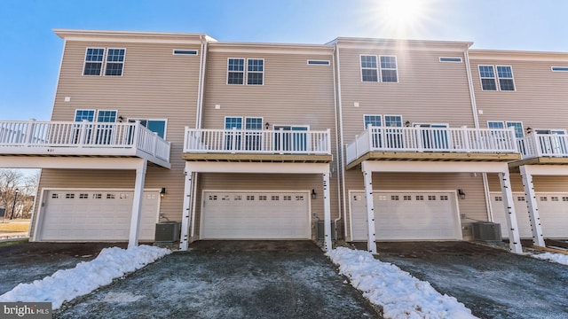 snow covered property with driveway, central AC, and an attached garage