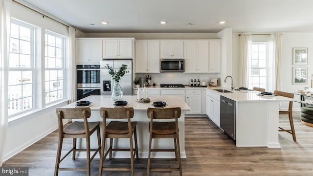 kitchen featuring a sink, stainless steel appliances, a breakfast bar, white cabinetry, and wood finished floors