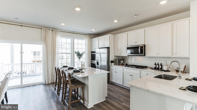 kitchen with a breakfast bar area, a sink, appliances with stainless steel finishes, dark wood finished floors, and backsplash