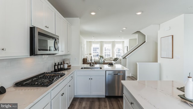 kitchen featuring white cabinets, a sink, appliances with stainless steel finishes, dark wood-style flooring, and a peninsula