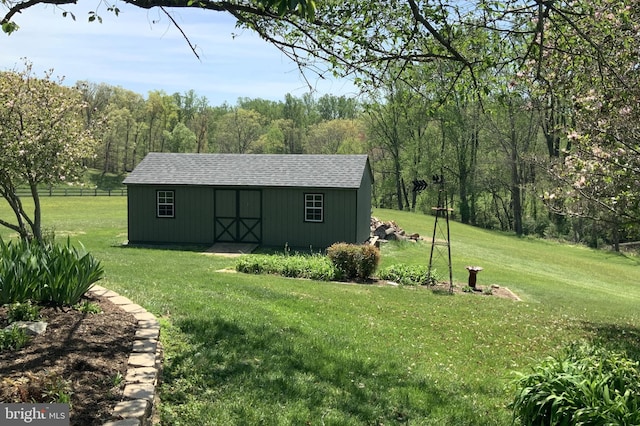 view of outdoor structure with fence, an outbuilding, and a wooded view
