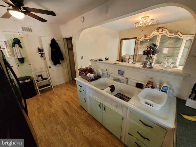 kitchen featuring arched walkways, light countertops, ceiling fan, a sink, and light wood-style floors
