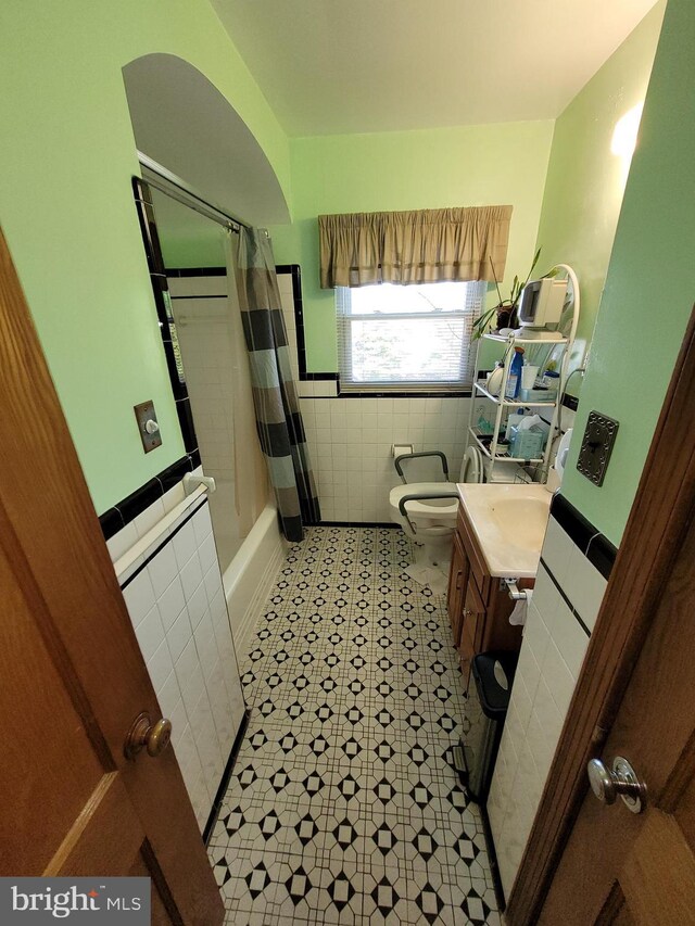 bathroom featuring tile walls, toilet, wainscoting, vanity, and shower / bath combination with curtain