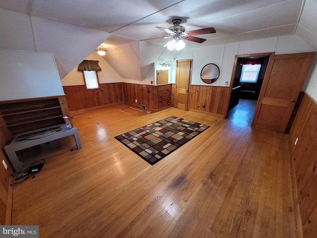 additional living space with light wood-style floors, wood walls, plenty of natural light, ceiling fan, and lofted ceiling