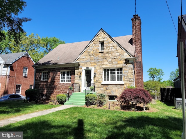 tudor-style house with a chimney, stone siding, and a front lawn
