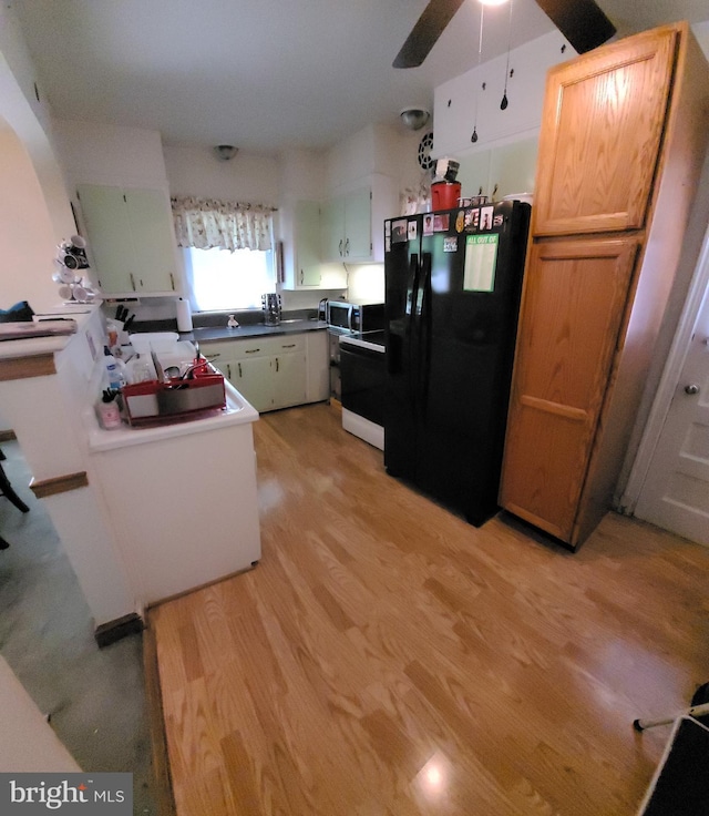 kitchen with black fridge with ice dispenser, light wood-style flooring, stainless steel microwave, a ceiling fan, and arched walkways