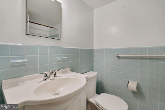 bathroom with tile walls, a wainscoted wall, toilet, and vanity