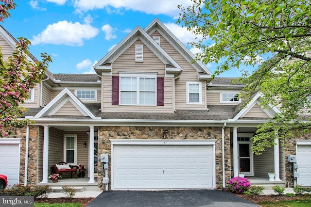 view of front of property featuring covered porch, stone siding, a shingled roof, an attached garage, and driveway
