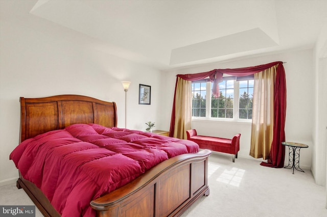 bedroom with a raised ceiling and light colored carpet