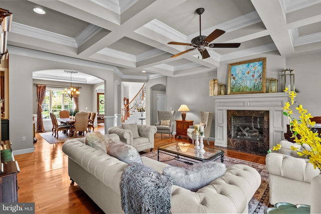 living room with arched walkways, coffered ceiling, ceiling fan with notable chandelier, and light wood-style flooring