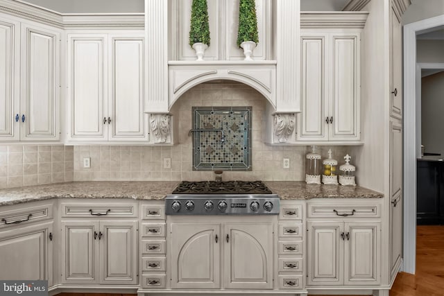 kitchen with stainless steel gas cooktop, light stone countertops, decorative backsplash, and wood finished floors
