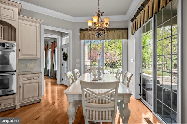 dining space featuring crown molding, a notable chandelier, visible vents, and light wood-style floors
