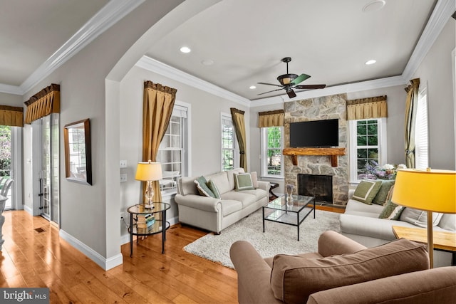 living room with a healthy amount of sunlight, arched walkways, a fireplace, and light wood finished floors
