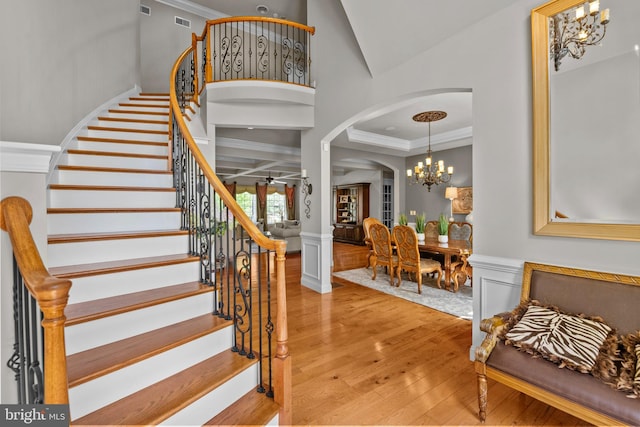 entrance foyer with wainscoting, wood-type flooring, arched walkways, ornamental molding, and stairway