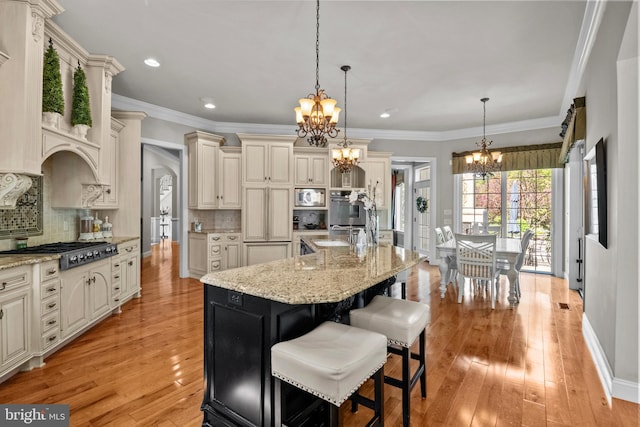 kitchen with cream cabinets, light stone countertops, appliances with stainless steel finishes, an inviting chandelier, and light wood-type flooring