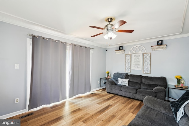 living area featuring ceiling fan, light wood finished floors, baseboards, visible vents, and ornamental molding