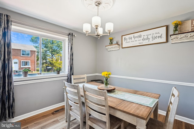 dining space featuring baseboards, wood finished floors, a notable chandelier, and visible vents