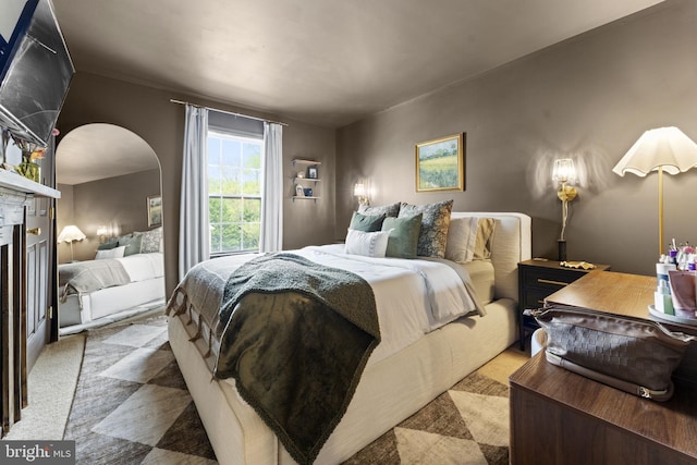 bedroom featuring carpet floors, arched walkways, and a fireplace