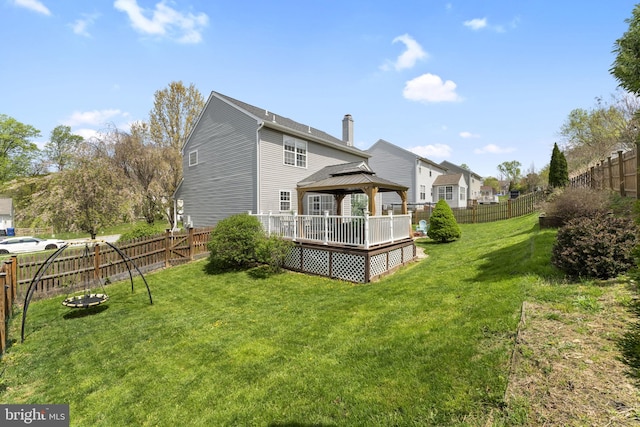 rear view of house with a chimney, a lawn, a wooden deck, a gazebo, and a fenced backyard