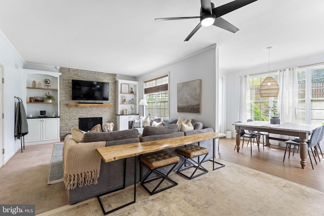 living room with crown molding, built in features, ceiling fan, and a fireplace