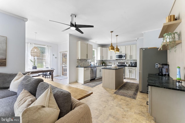 kitchen with dark countertops, a center island, stainless steel appliances, open floor plan, and ornamental molding