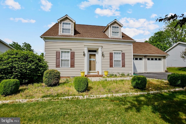 new england style home featuring roof with shingles, a front yard, driveway, and a garage