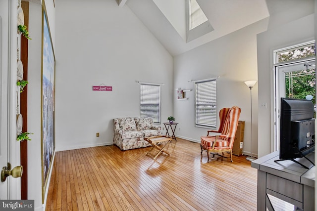 sitting room with light wood-type flooring, baseboards, a skylight, and high vaulted ceiling