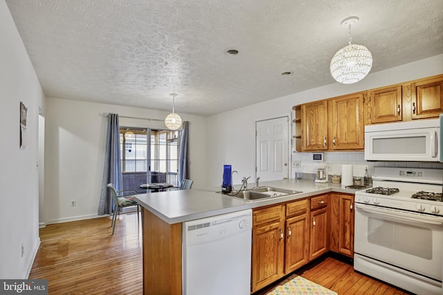 kitchen with a sink, a textured ceiling, a peninsula, and white appliances