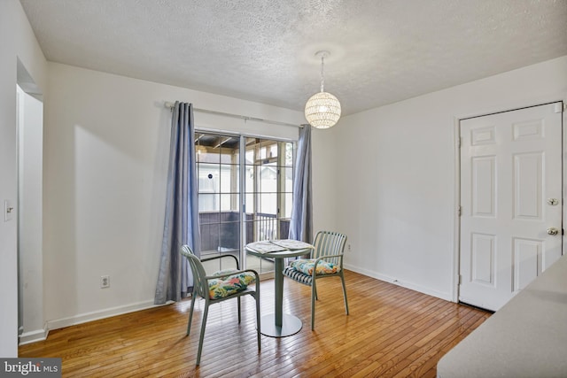 dining room featuring baseboards, hardwood / wood-style flooring, a textured ceiling, and a notable chandelier