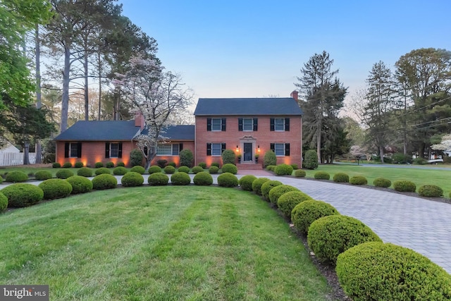 colonial house featuring brick siding, a front yard, and a chimney