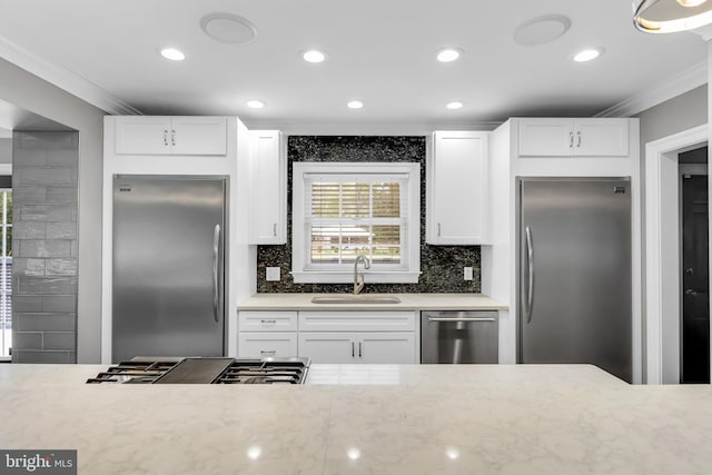 kitchen featuring crown molding, white cabinets, appliances with stainless steel finishes, a sink, and backsplash