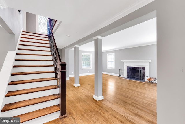 stairway featuring crown molding, a fireplace, baseboards, decorative columns, and wood finished floors