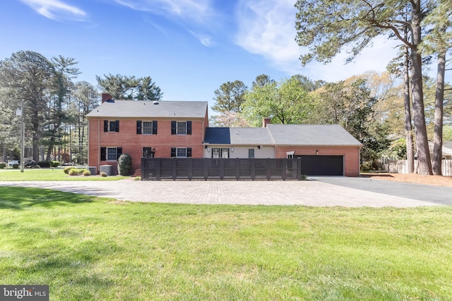 colonial-style house with a garage, a chimney, a front yard, and brick siding