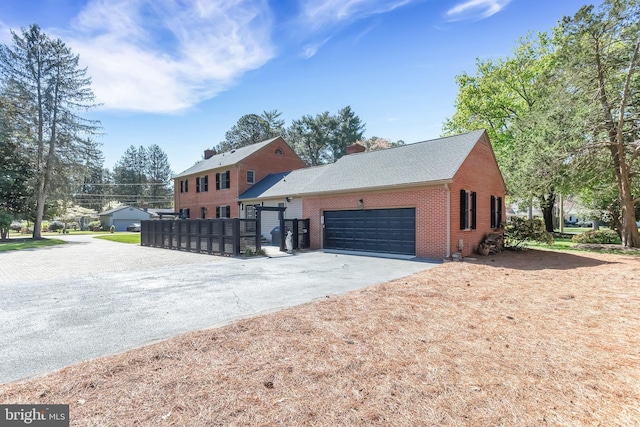 view of front of house with brick siding, an attached garage, aphalt driveway, and a chimney